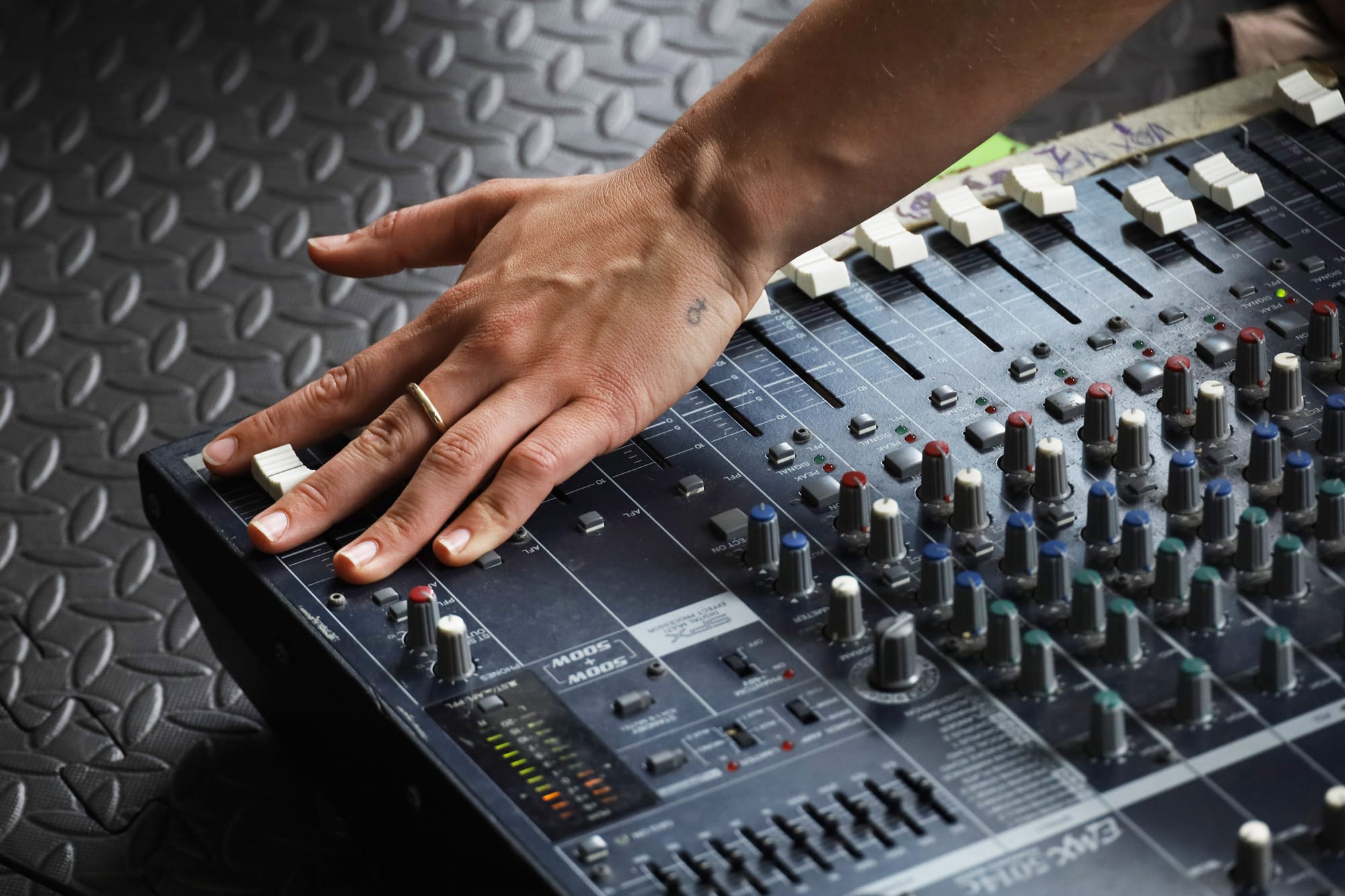 A fair-skinned hand modulates a channel button on a venue mixing board.